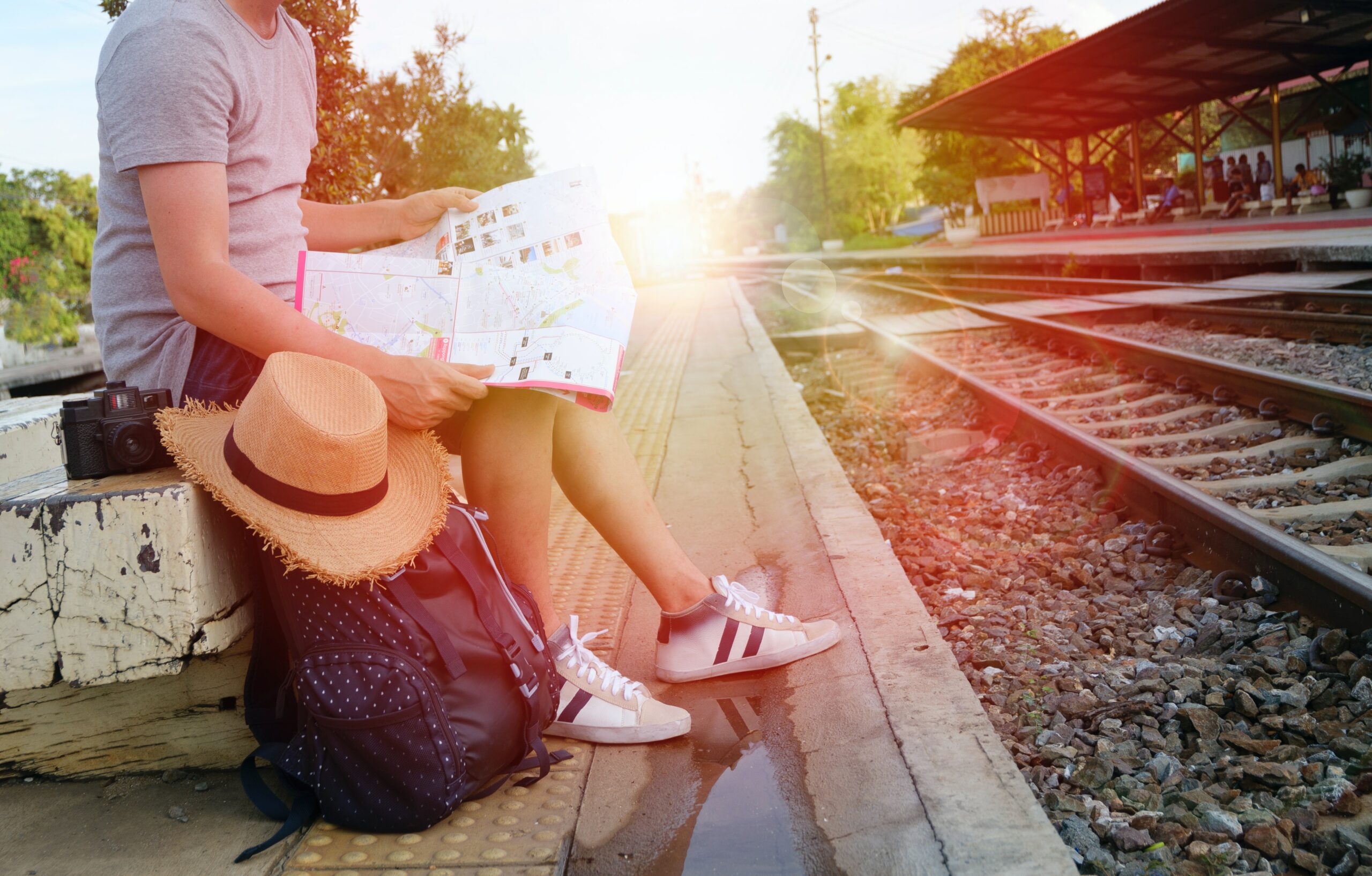 Image of a tourist at a train station, carrying a small backpack, and a looking at a map.