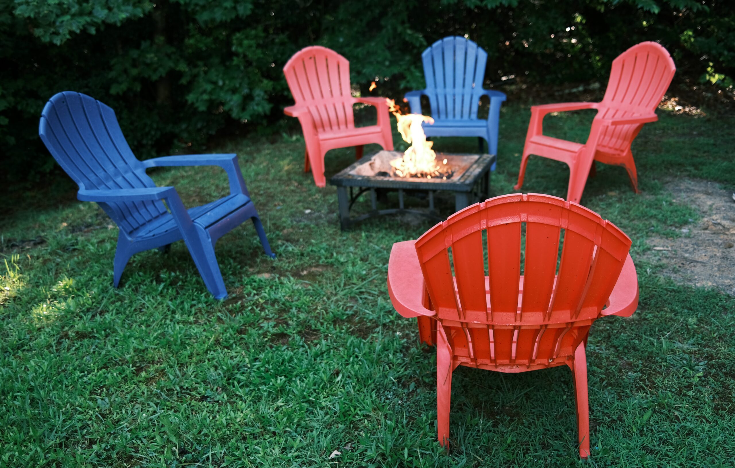 Image of a backyard with blue and red patio chairs and fireplace located in the middle