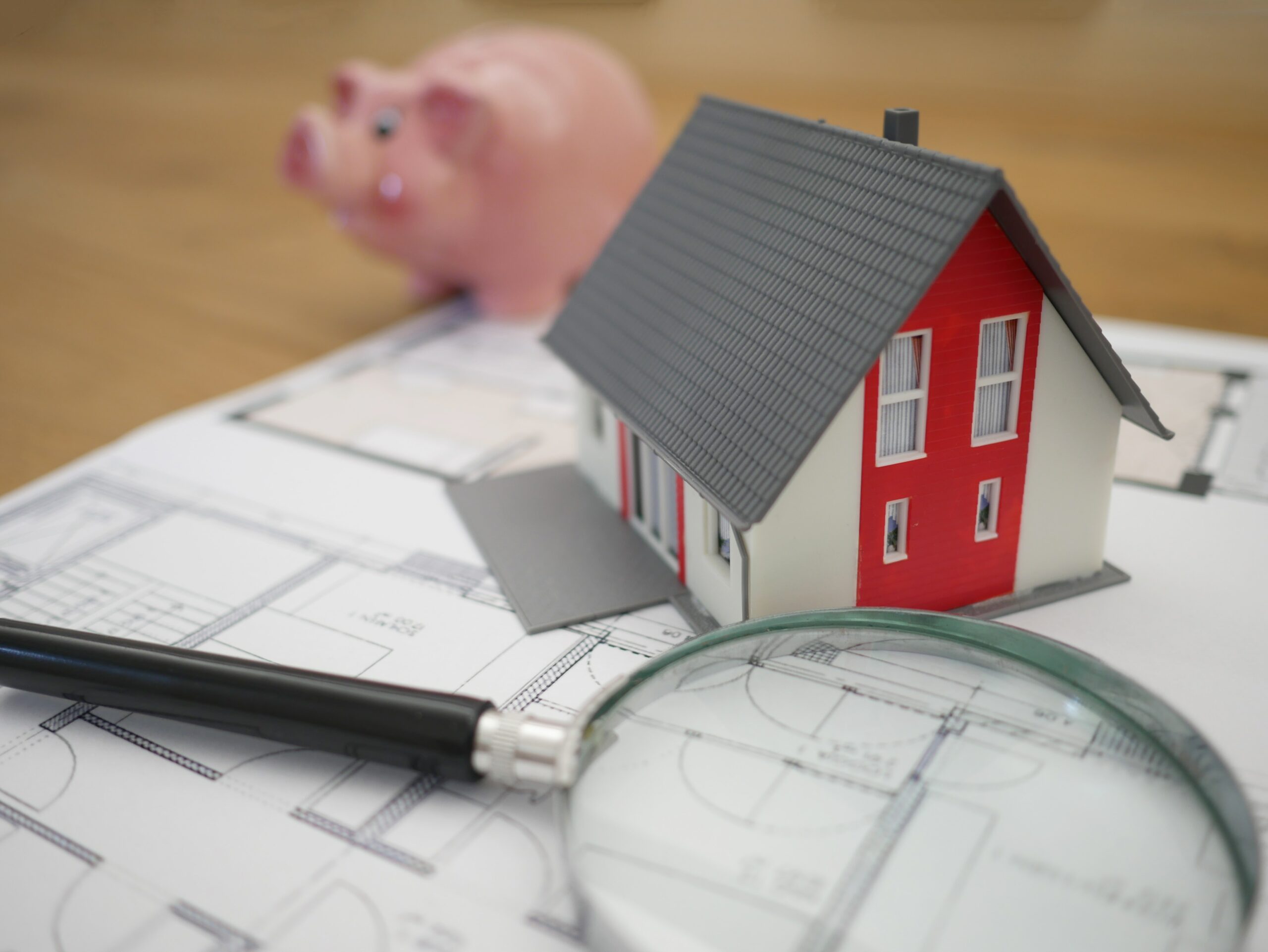 Image of a house floorplan, miniature home, and a piggy bank to emphasize that property managers must be knowlegable in real estate.